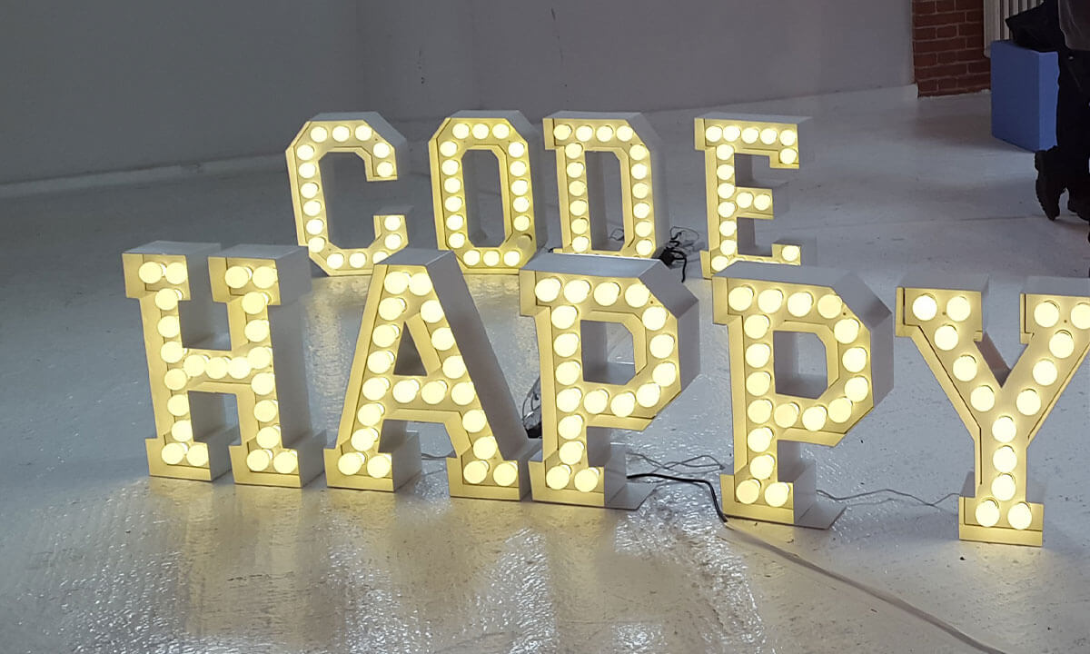 Sfeerfoto van lichtgevende letters op een betonnen vloer, er staat: code happy